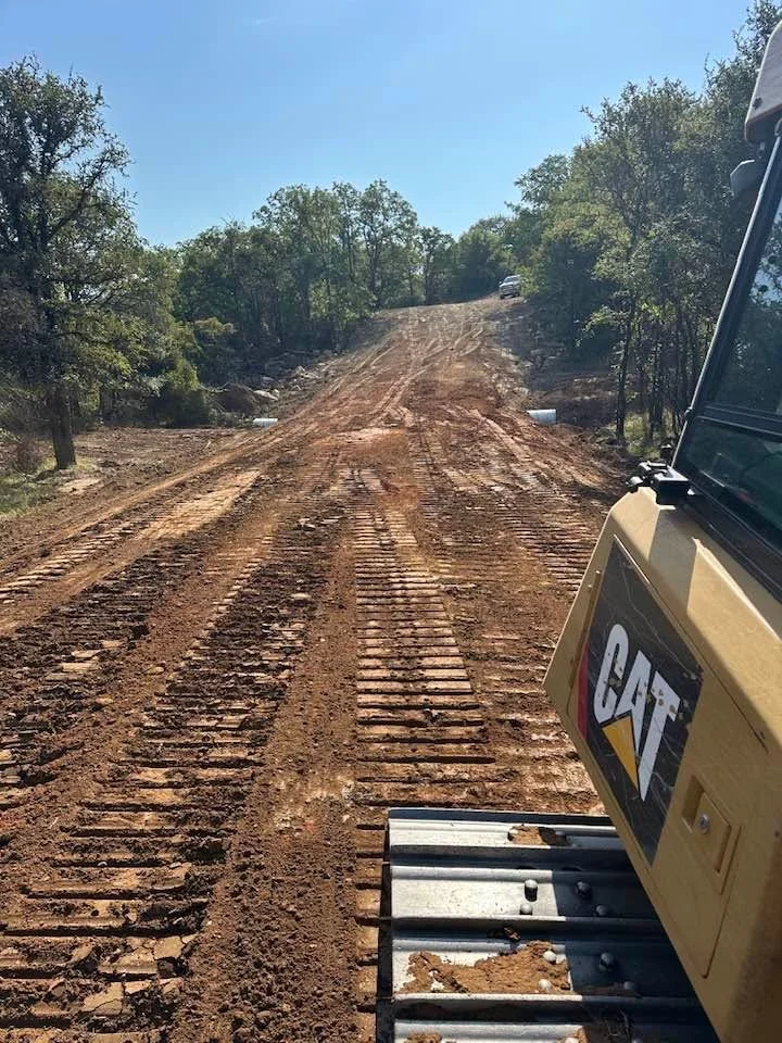 Excavated dirt driveway with blade marks, heavy equipment visible, wooded property