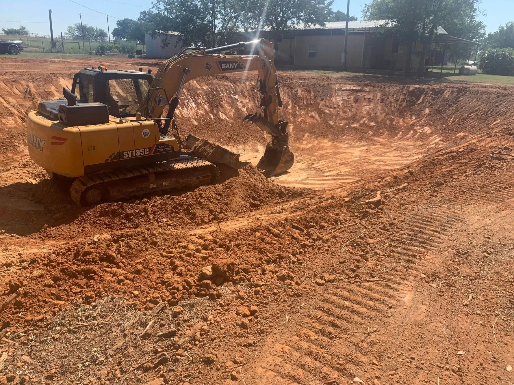 SANY excavator digging and grading red clay soil on residential property
