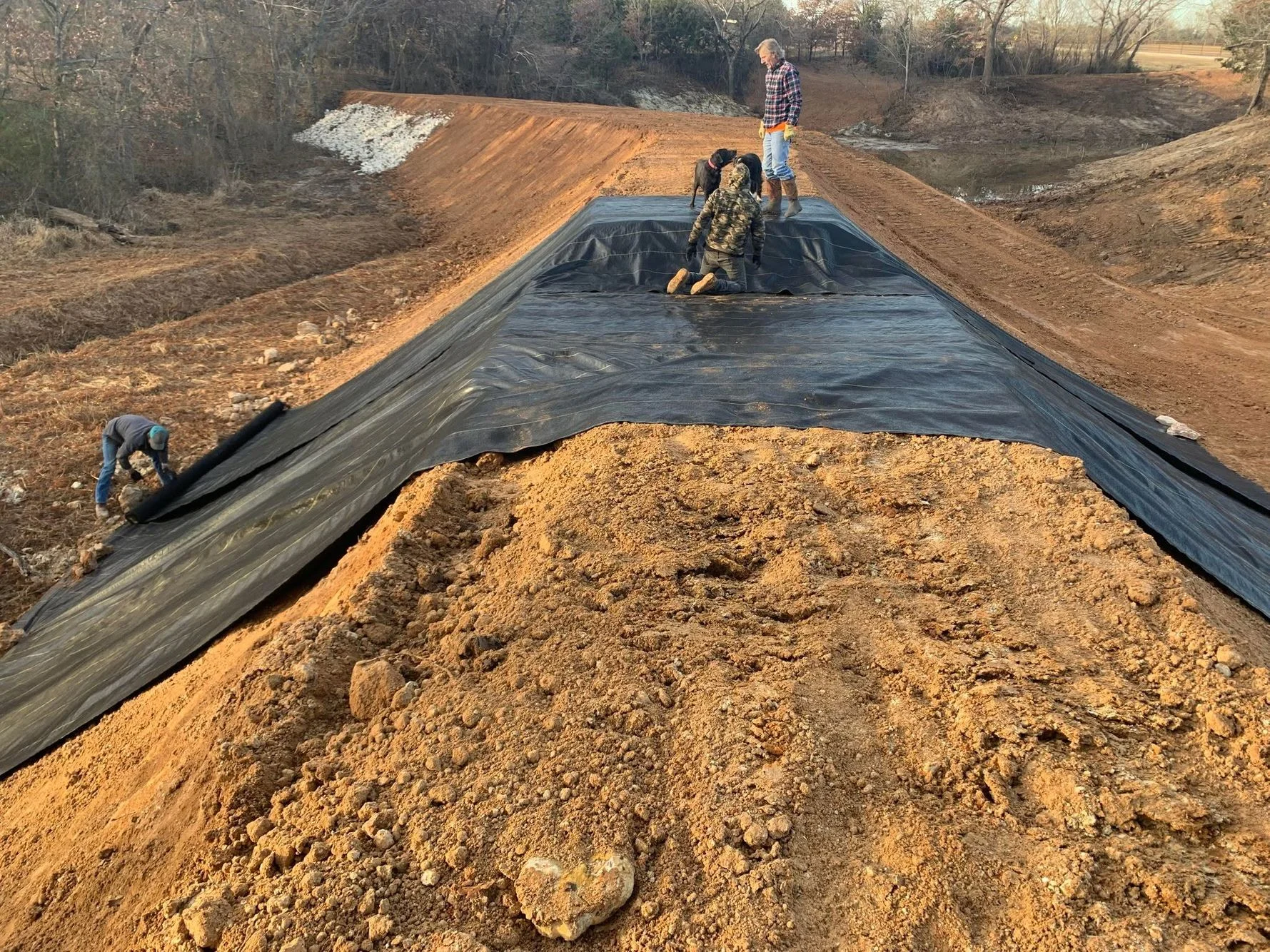 Pond excavation with black HDPE liner, graded dirt banks, and site preparation work