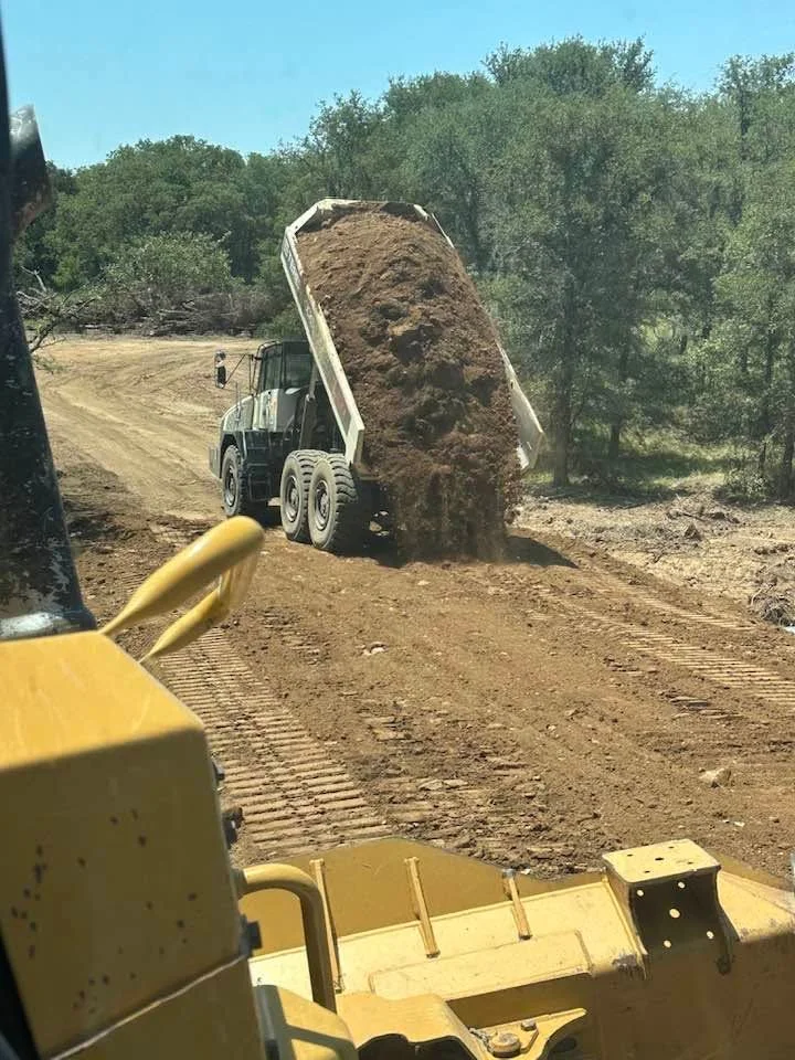 Dump truck unloading topsoil and aggregate material at job site with heavy equipment
