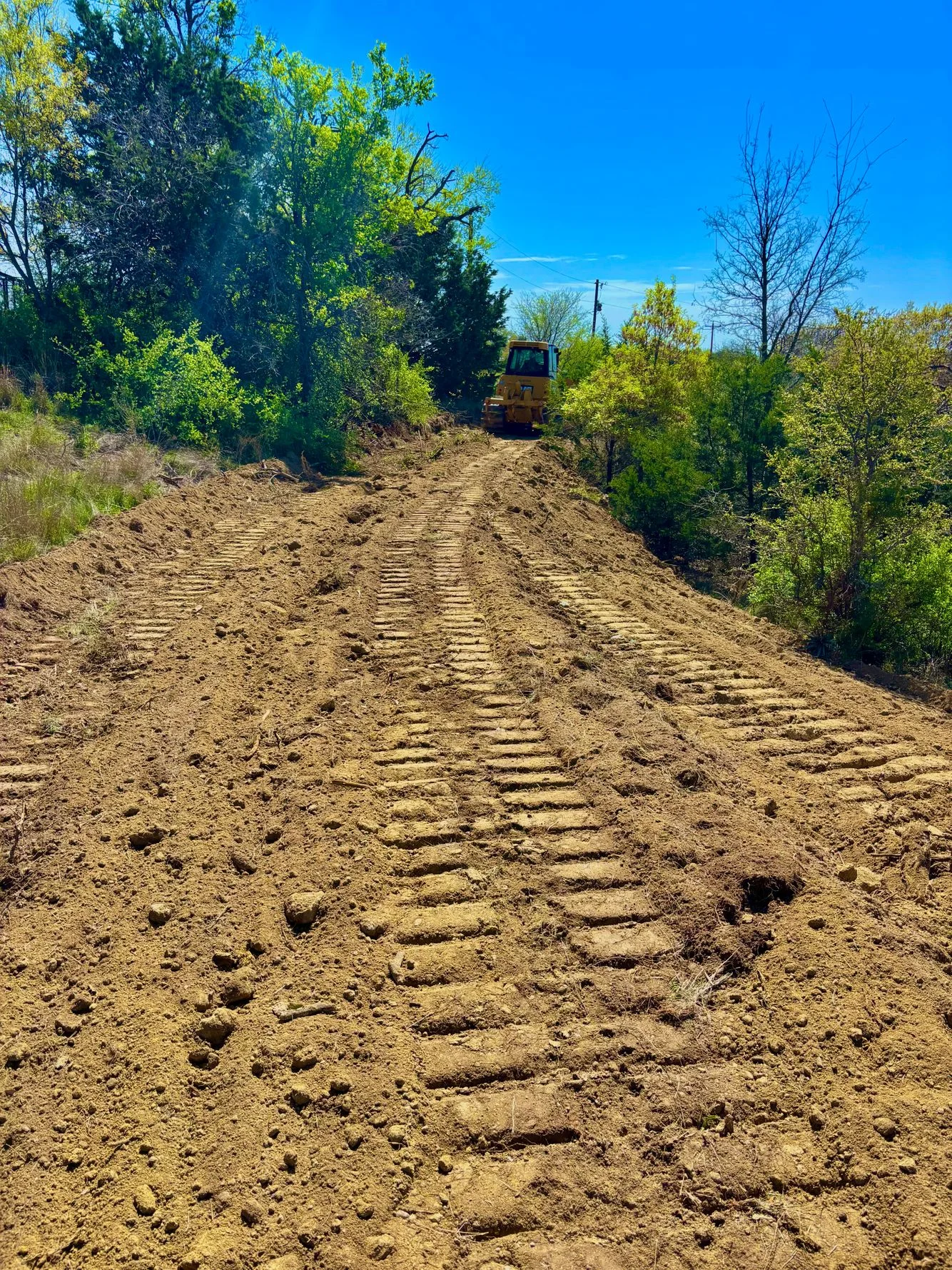Graded dirt driveway with compacted soil and dozer tracks on sloped terrain