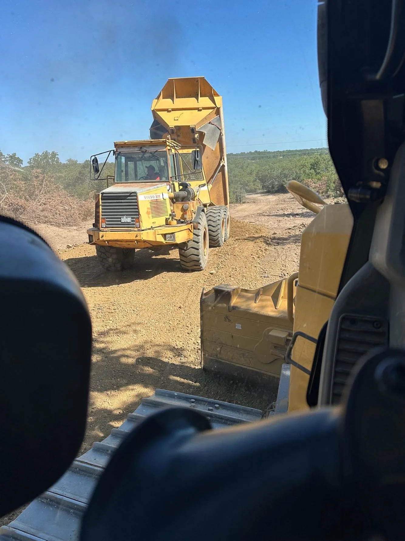 Yellow dump truck and excavator on dirt site during earth moving and grading work