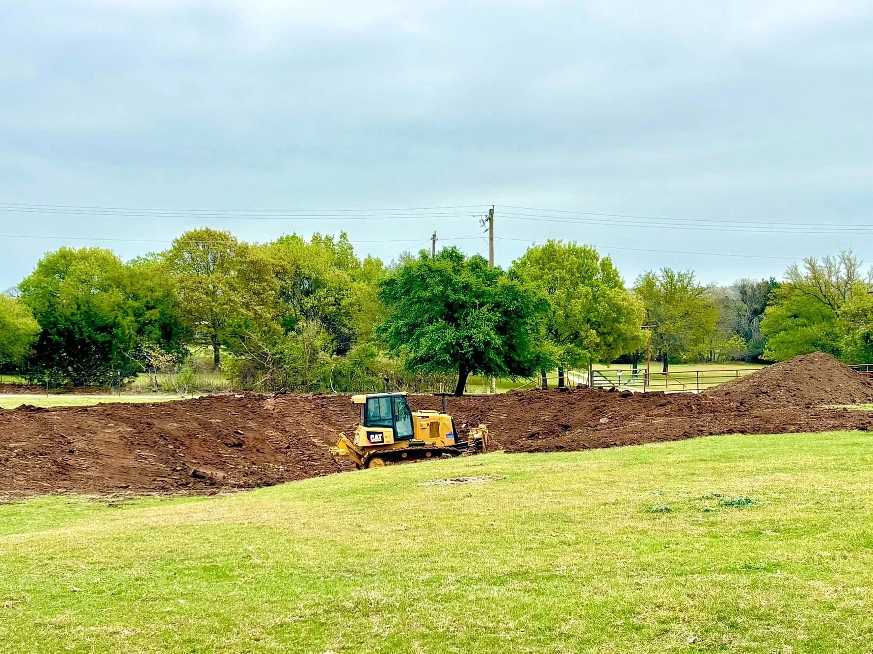 CAT tracked dozer grading and compacting soil on rural property with trees in background