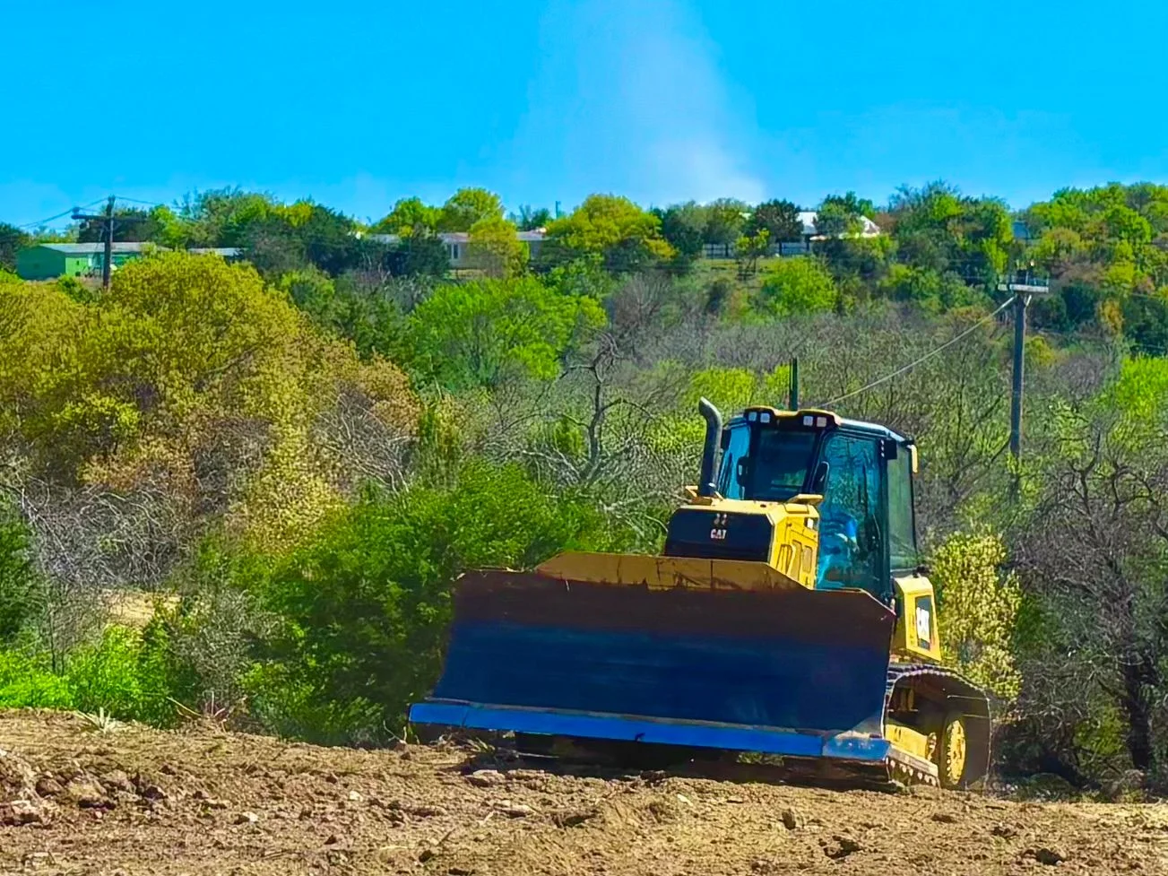 CAT track loader with blue push blade clearing dense brush and vegetation from residential land