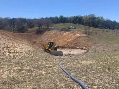 Excavator grading sloped terrain with drainage pipe installation and site preparation work