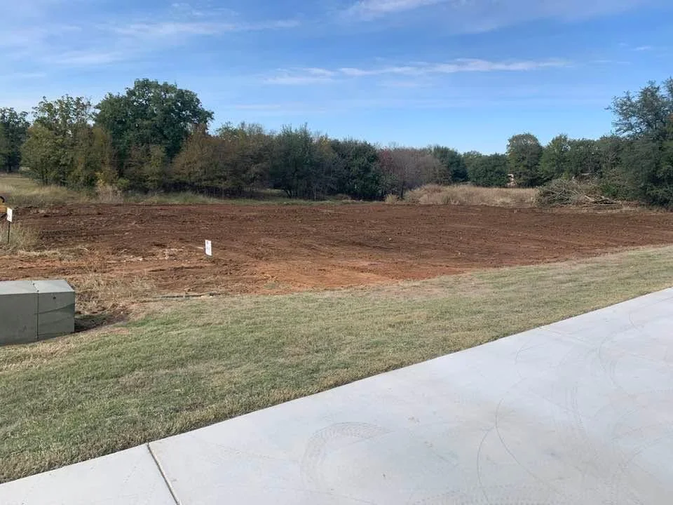 Excavated residential lot with graded subsoil, concrete pad, and lawn transition